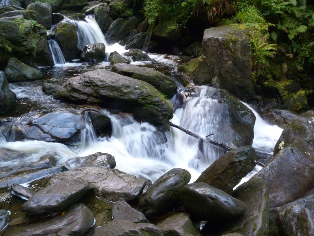 Closeup eines Wasserfalls in Wales, das Wasser strömt über dunkle, nasse und teils moosbewachsene Steine