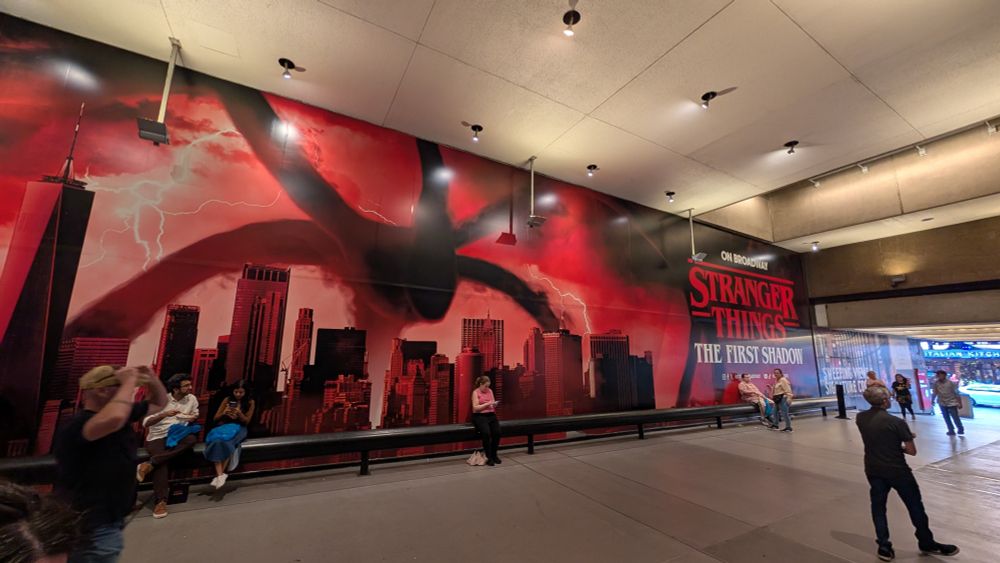 A wall outside the theatre promoting "Stranger Things: The First Shadow" along with a massive mural of the NYC skyline tinted red and a Mind Flayer stalking over it.