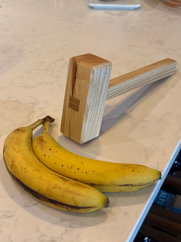 A wooden mallet and two bananas on a quartz countertop. 
