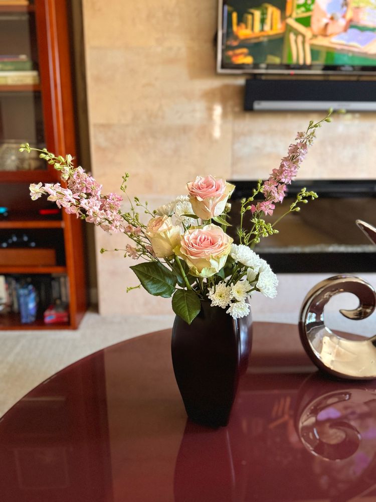 Pink, cream and green flowers in a dark tall vase on a round burgundy table. 