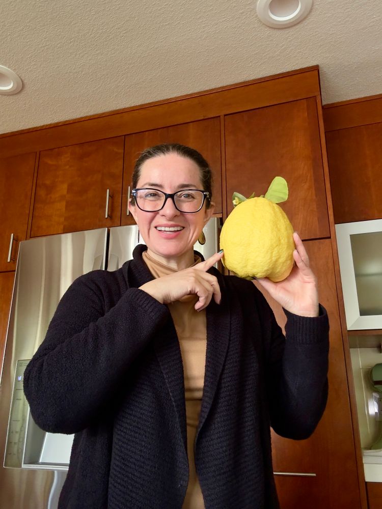 Woman in a black sweater holding a very large citron lemon in her hand