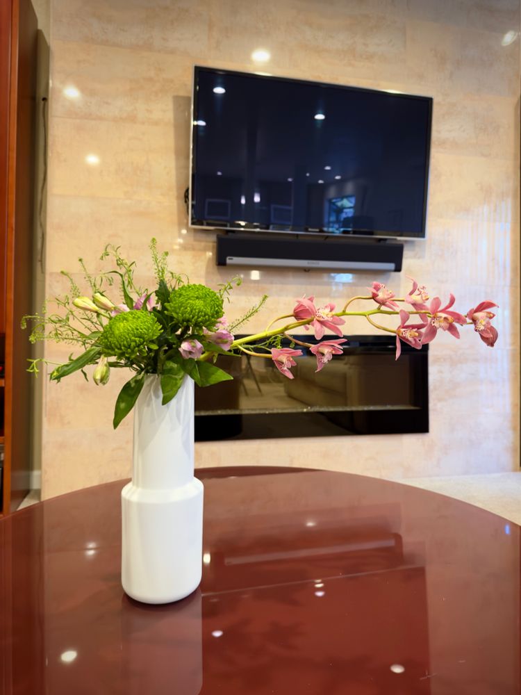 Japanese Ikebana floral arrangement of green and pink on a round brown table. 