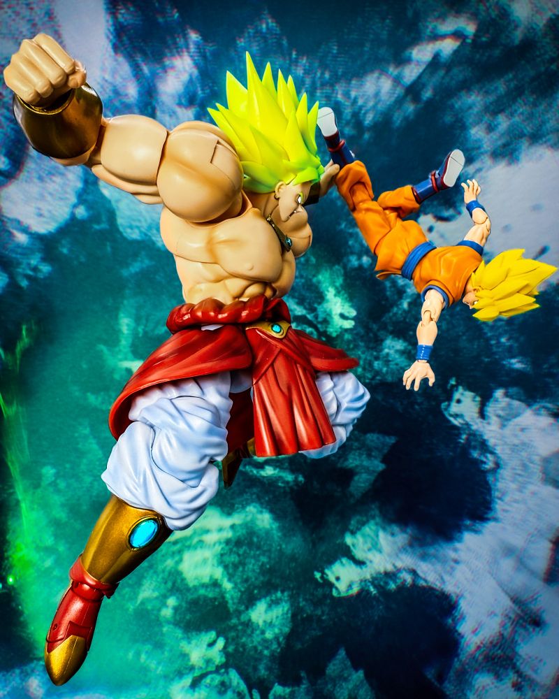 An edited photograph of the Demoniacal Fit third-party release of S.H.Figuarts Broly from Dragon Ball Z. The figure is radiating with a greenish aura. Broly has grabbed Goku's leg and is pulling his weakened body towards him as he charges a punch. His power is maximum.