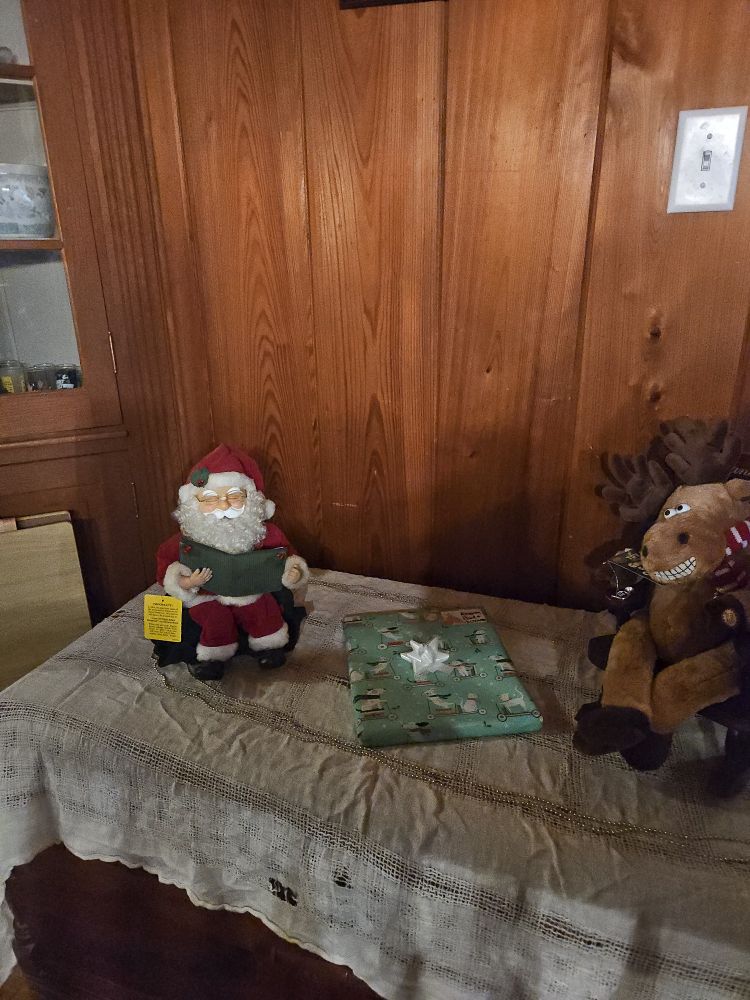 presents table with santa in a recliner decoration and reindeer in a rocking chair decoration on opposite sides of the present 