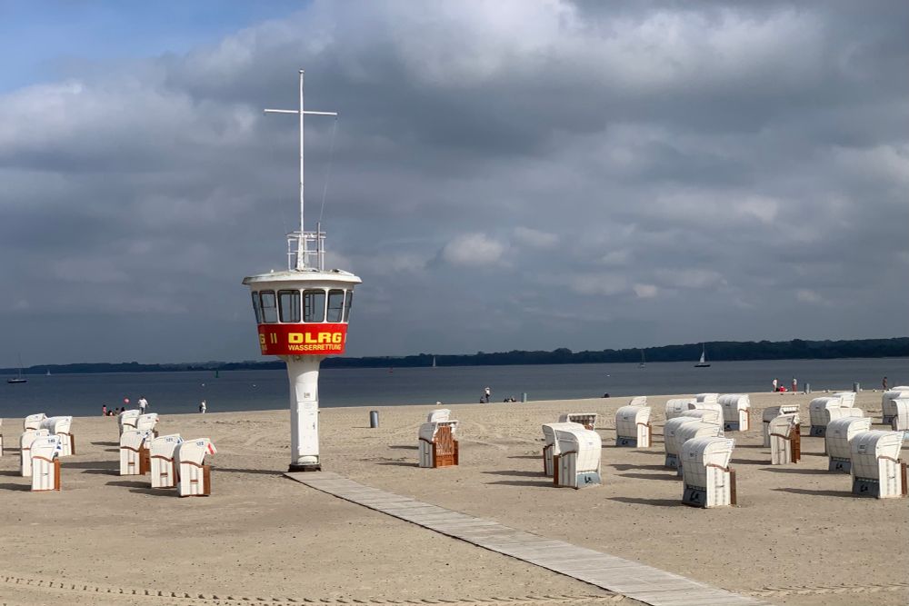 Ein DLRG Aufsichtsrurm steht am Strand, umringt von Strandkörben. 