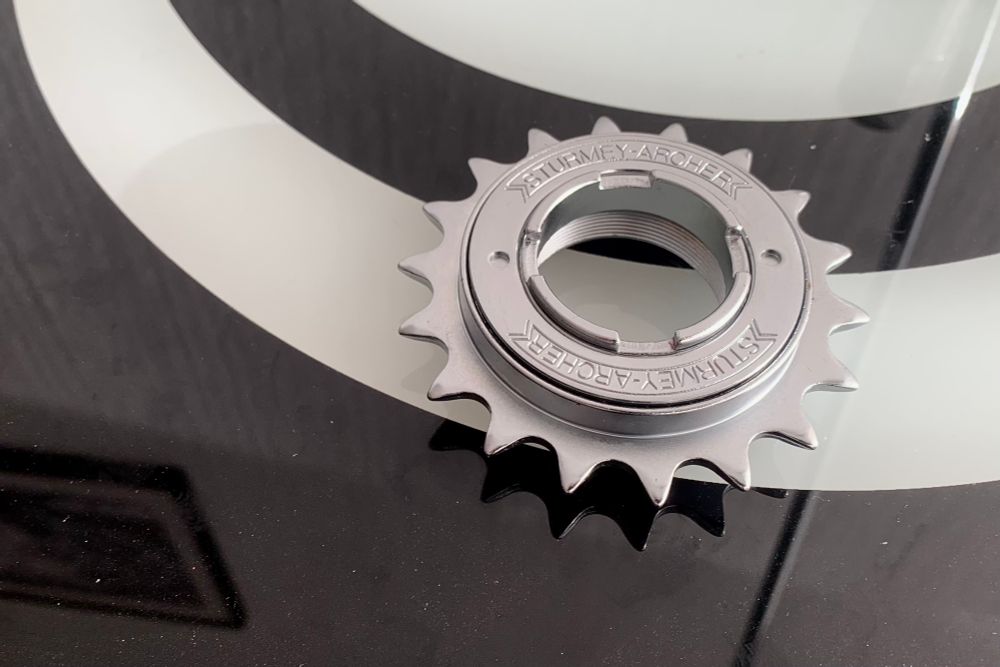 Ein Freilaufritzel liegt auf einem exzentrisch gemustertem schwarz weiß Glastisch. 