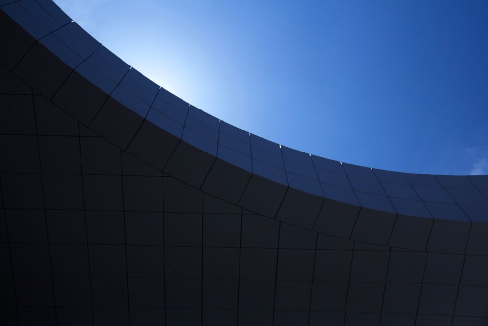 vibrant blue sky, a curve of white metal tiled panels masks the sun and appears dark blue from the shadow