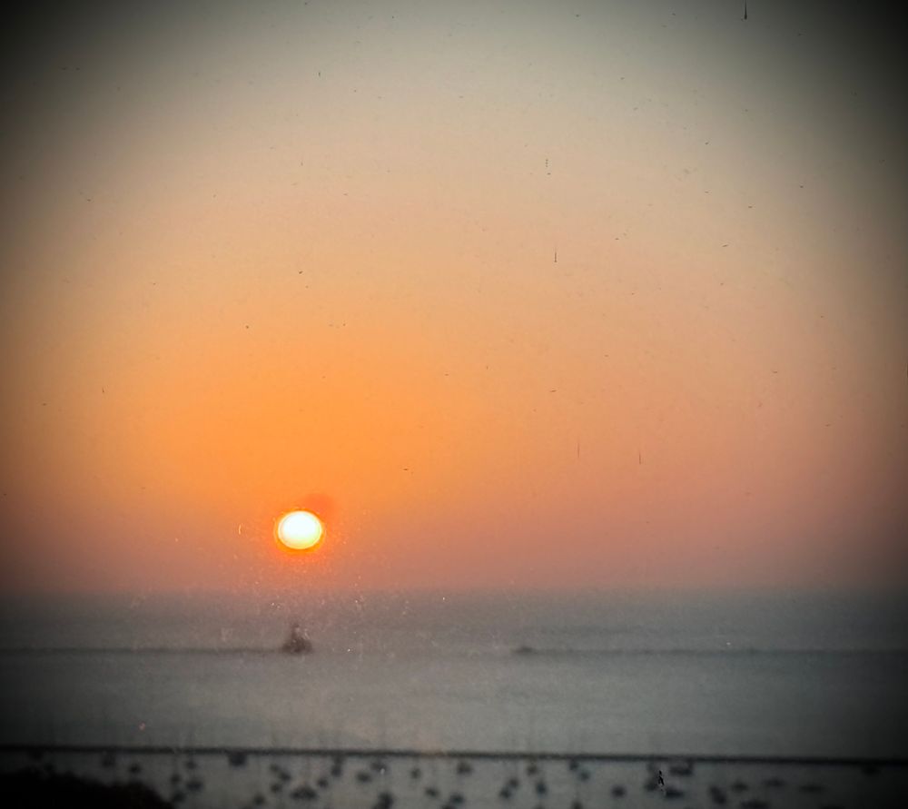 blurry, grainy sunrise over a body of water stretching to the horizon with a marina in the foreground 