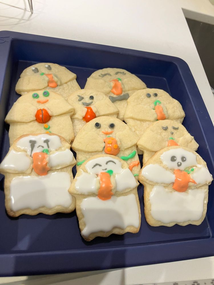 ghost sugar cookies holding pumpkins decorated with white, grey, green, & orange icing 