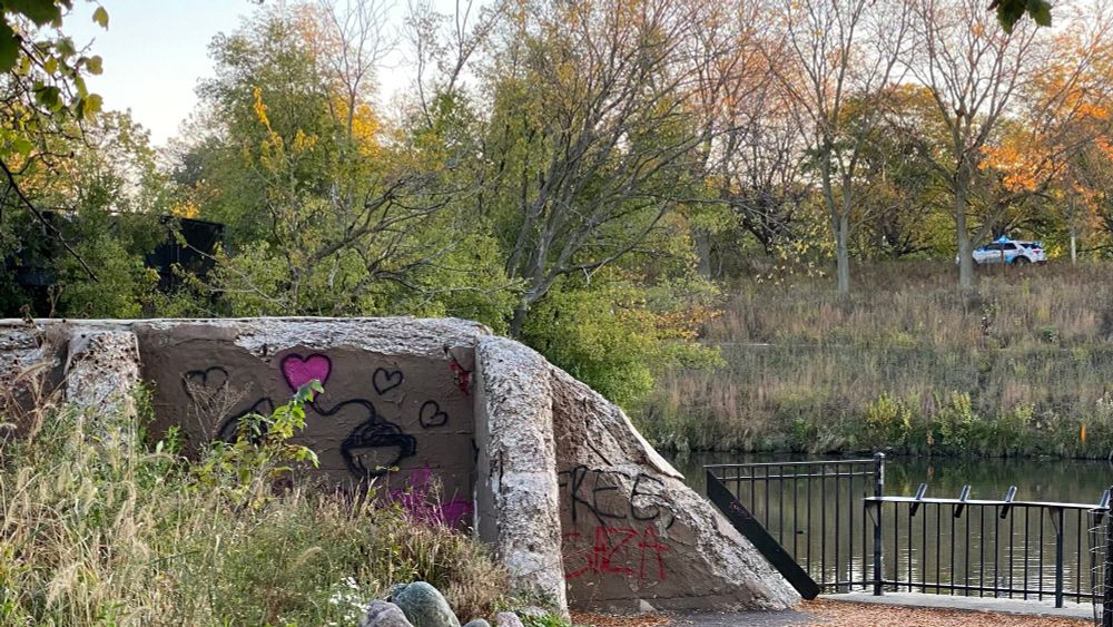 Photo of Chicago River. On the opposite side, a CPD SUV is driving down the running and biking path. Blue light on. As always. Because that’s how they do. Sunday, October 26, 2025 7:47 am. 