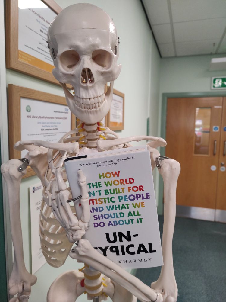 Photograph of a skeleton holding the book "Untypical"