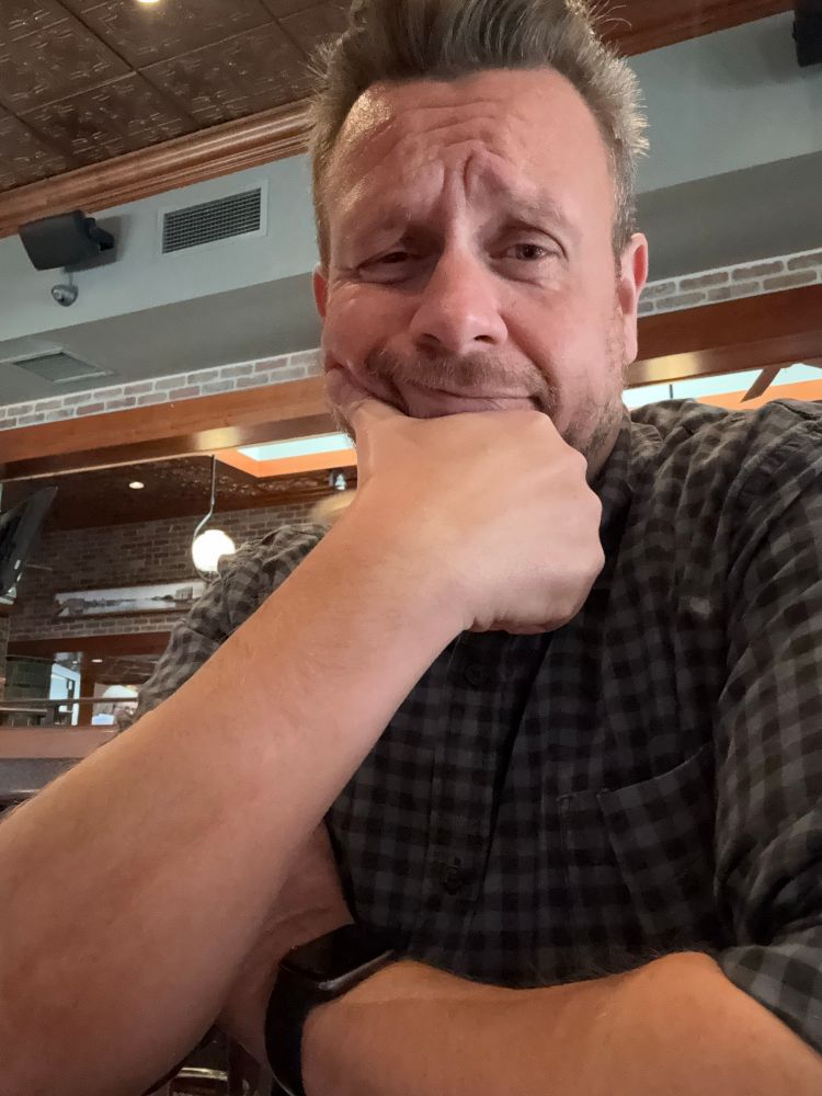 Me with a slightly confused face baring my forearm in my blue flannel shirt.