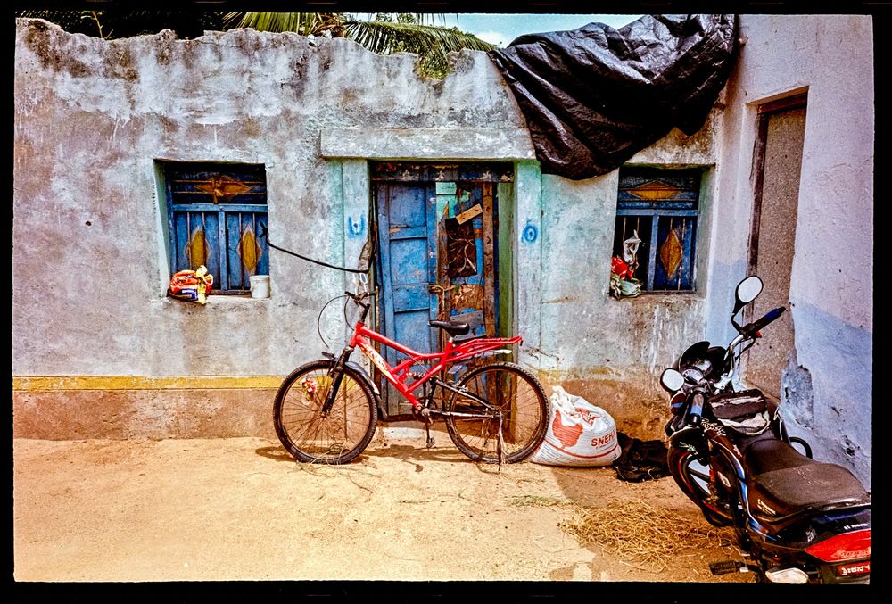 A run down house with a blue door, and a red bike parked in front. 