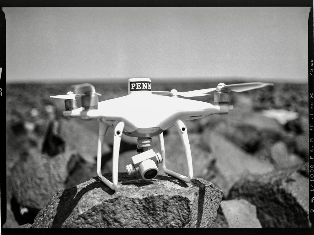 A white drone sits on a black boulder. 