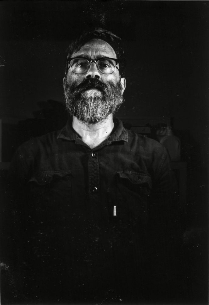 Black and white photo of a bearded man, with just his head lit by strobes against a black background. 