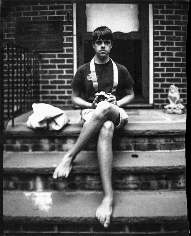 Contrasty black and white image of a young man sitting on a stoop holding an slr. 