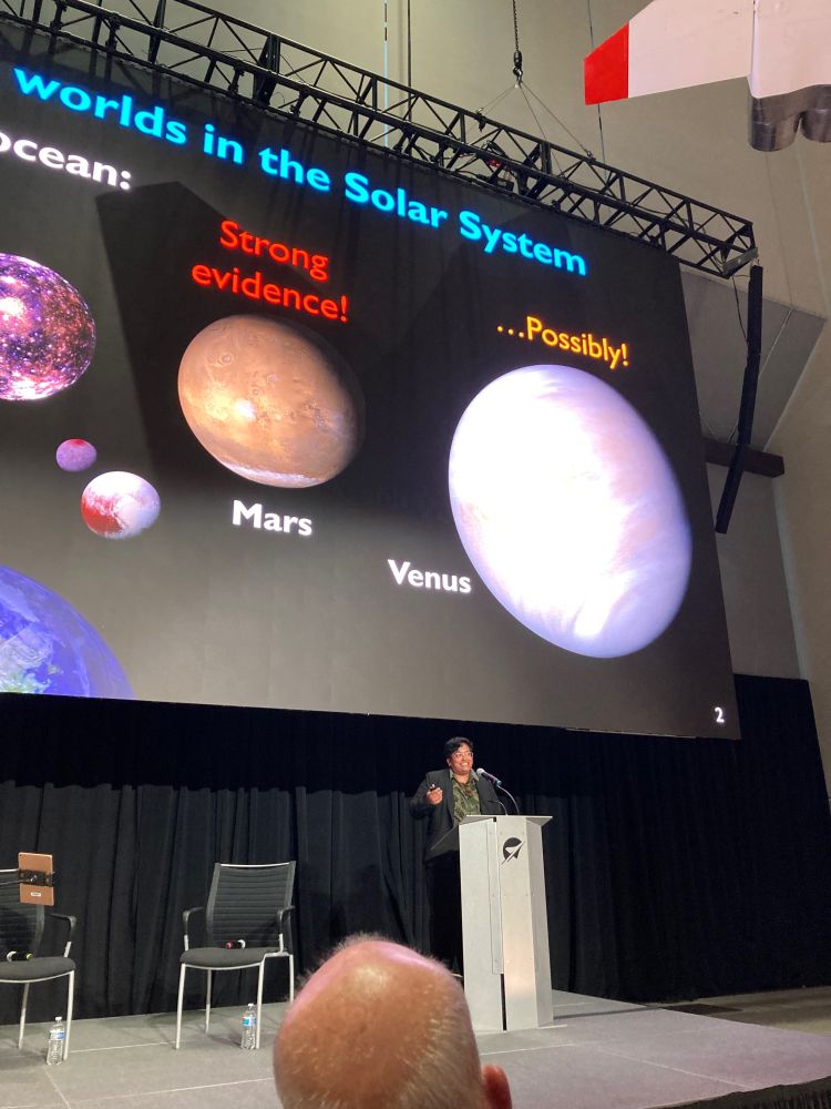 Rita Parai at the podium in front of a slide surveying oceans in the solar system. 