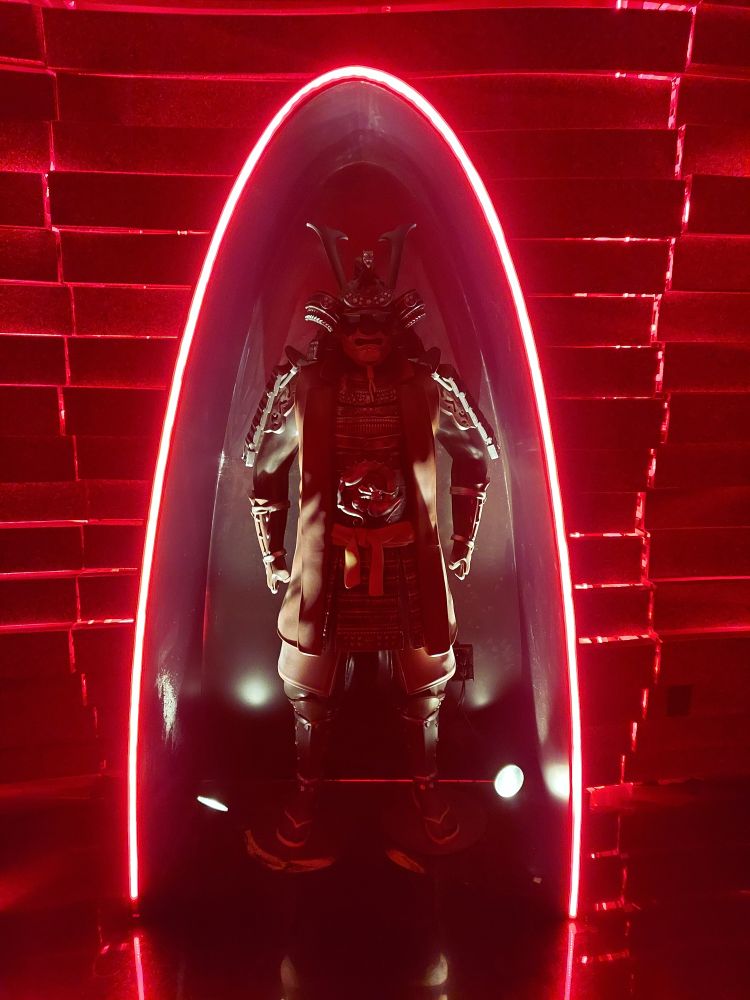 A samurai statue standing within a neon light fixture. Everything is very red. 