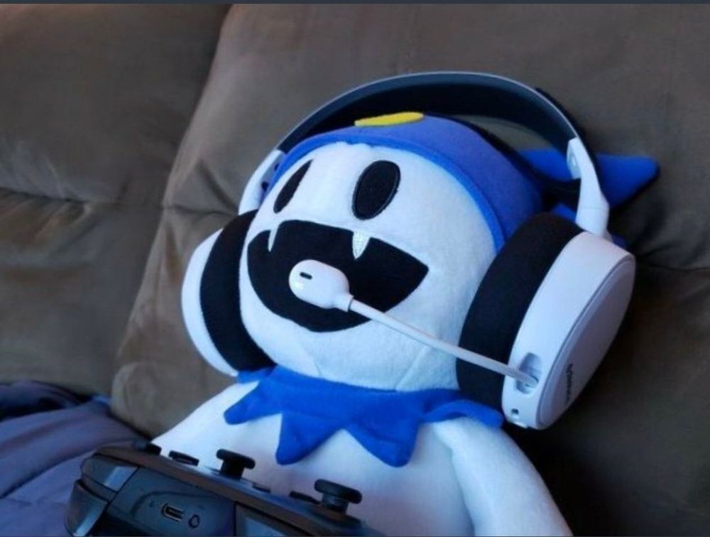 A Jack Frost plush sitting on a couch with a Nintendo Switch Pro Controller and a headset