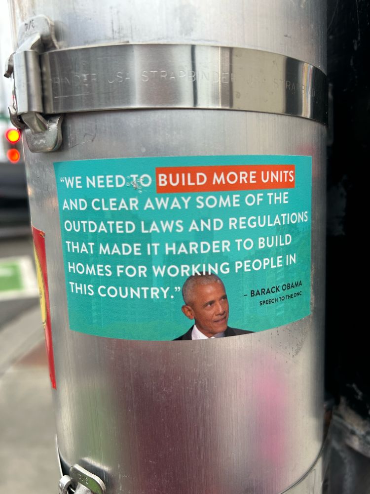 Sticker on a pole with an Obama quote that says “We need to build more units and clear away some of the outdated laws and regulations that made it harder to build homes for working people in this country.”