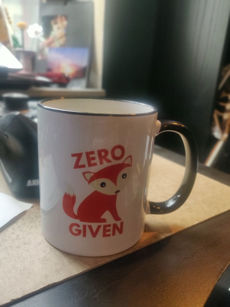 Eine Tasse, die einen Fuchs darstellt. Über dem Fuchs steht in englisch Zero und unter dem Fuchs, ebenfalls auf englisch, Given. Es liest sich als 'zero fox given'.