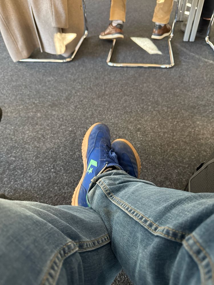 Foto von blauen Converse Sneakern die sich nur leicht vom Industrieteppichboden des Seminarraums der KV abheben. Pfeil und Stern in Türkis auf den Schuhen.