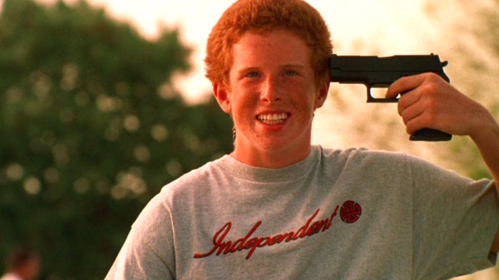 ein grinsender rothaariger teenager hält sich eine pistole an den kopf
