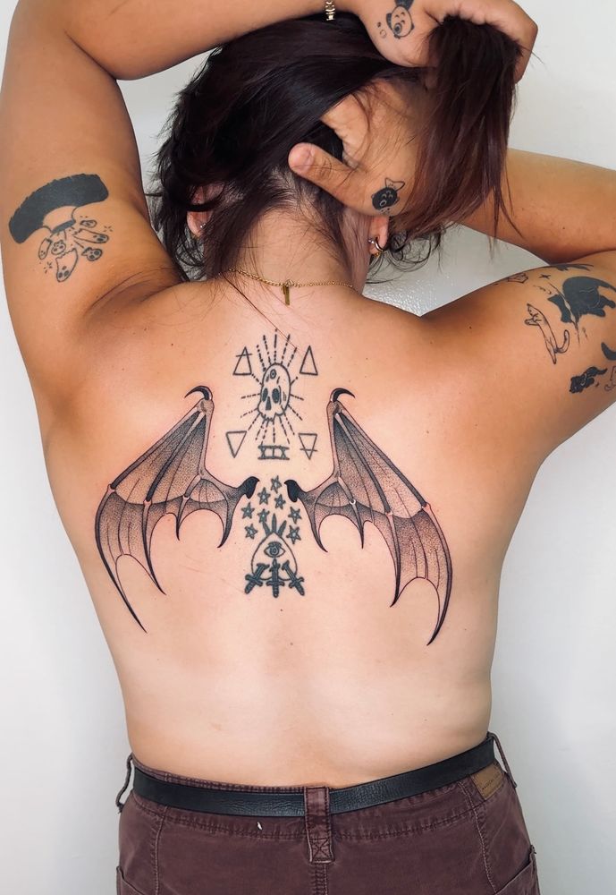 Jorah's back tattoos. This photo is completely safe for work. Woman's back displaying new Bat Wing tattoos.
Between the bat wings are a skull with the alchemical symbol for the sun on it's forehead, 8 Pentacles, and an inverted 3 of swords.