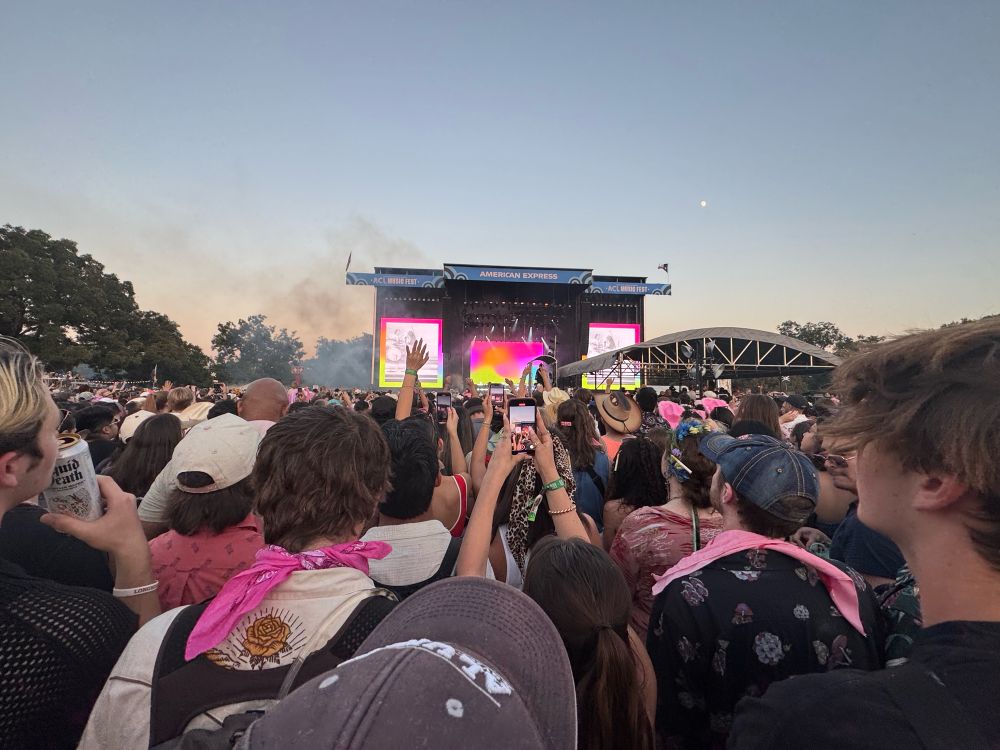 Concert photo, stage in the distance, lots of pink throughout the crowd. Clearly at a music festival and outdoors.
