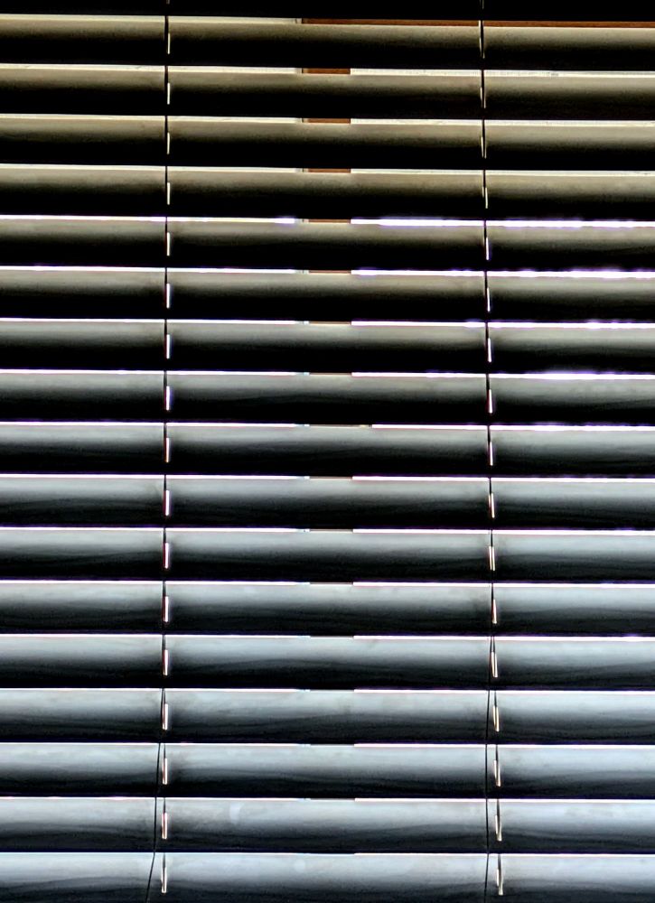 Close-up of closed Venetian blinds letting in a little sunlight on a fair autumn morning.