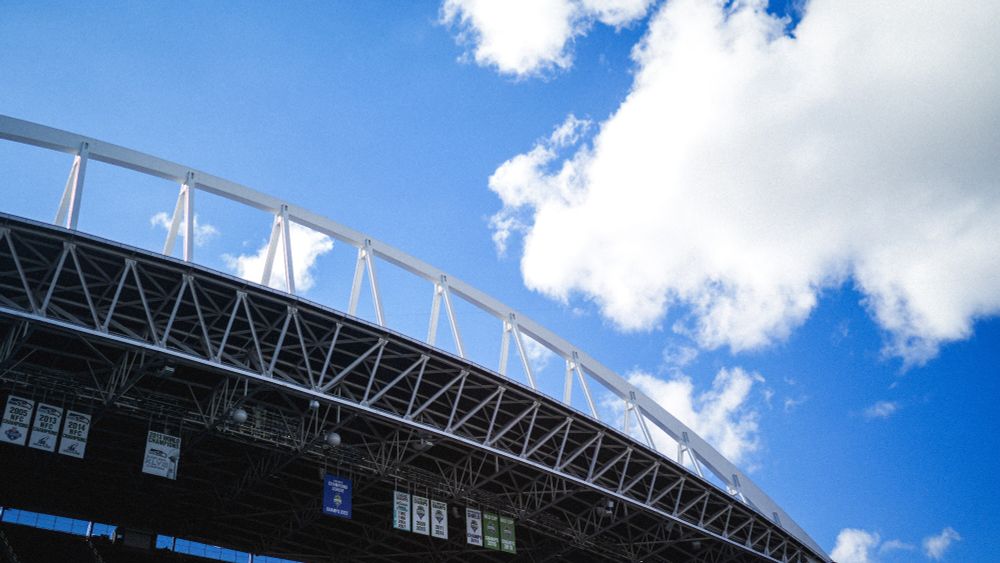 An image of the arches above Lumen Field with blue skies and white clouds behind them.