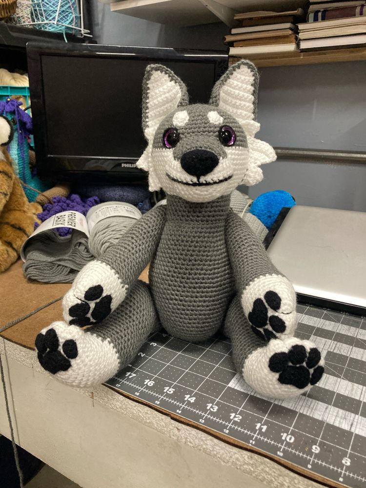Gray and white crochet wolf sitting on a messy desk