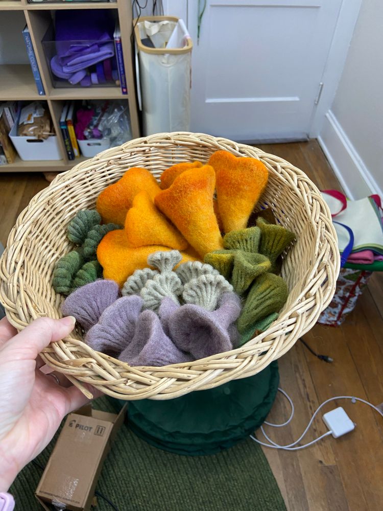 A light colored wicker basket with an assortment of colorful needle felted mushrooms 