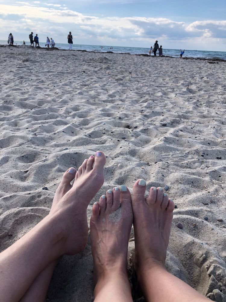 Zwei paar Füße mit lackierten Fußnägeln im Strandsand. 