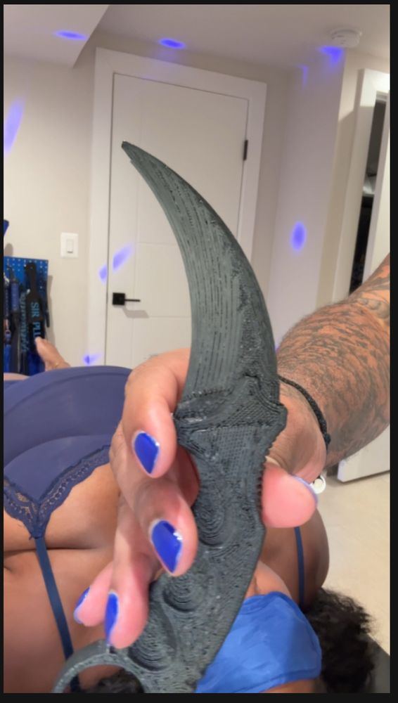 Black 3-d printed knife in the hands of a man with blue nails. 
