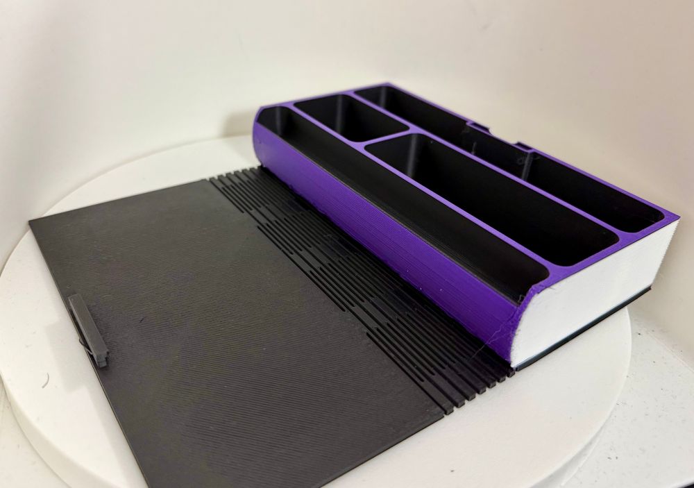 Picture of a black, purple, and white DnD accessories box. It is made to look like a book. 