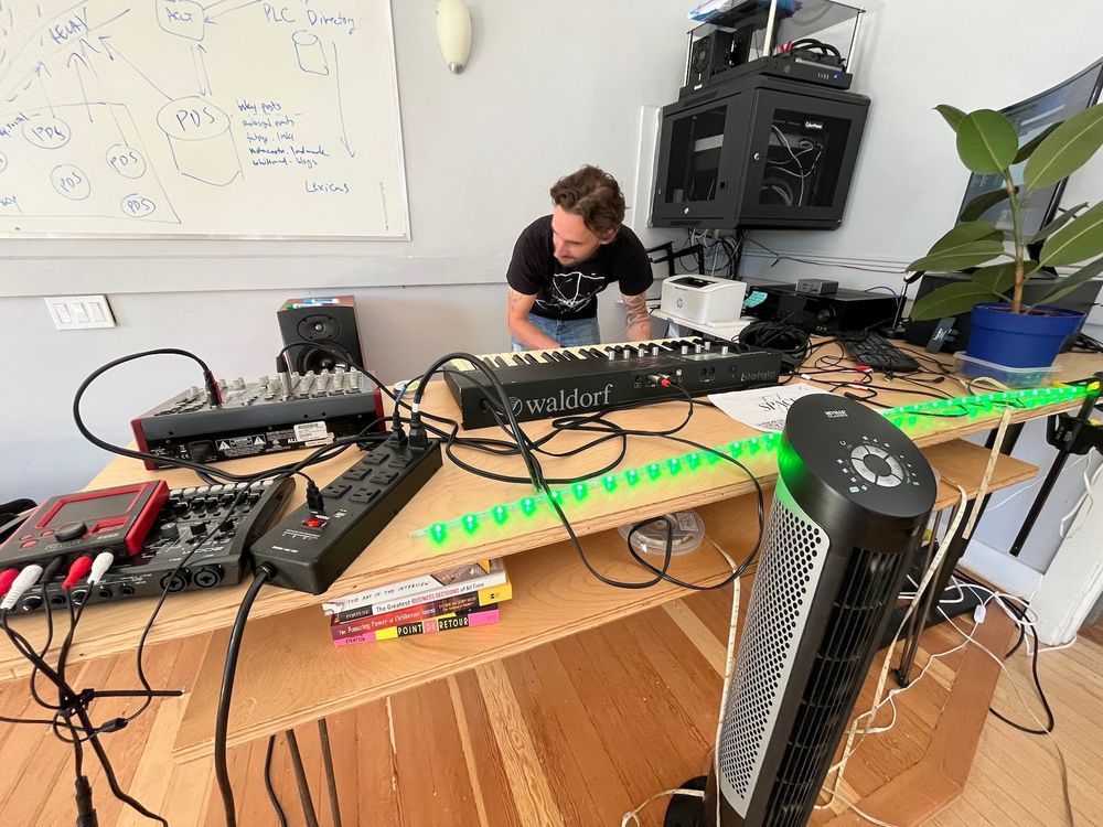 David sets up synths and mixer at the front of the room. A whiteboard contains PDS notes.