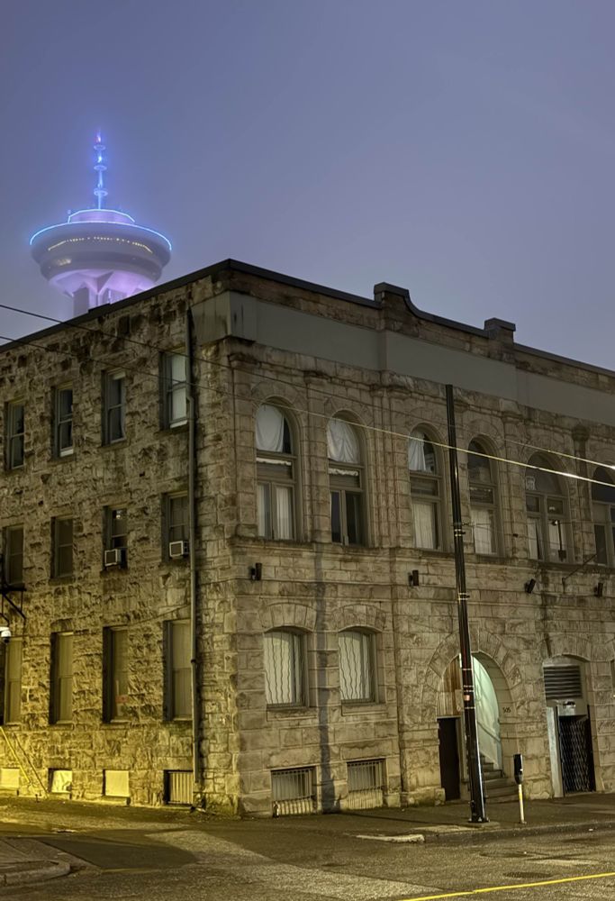 A view of 505 Hamilton entrance stairs and our studio with the yellow sodium alley light. There are blue lights highlighting the Harbour Centre Lookout Tower above the building, with some mist and fog in the air. Photo by Jonny Ostrem @jonny.z-space.ca