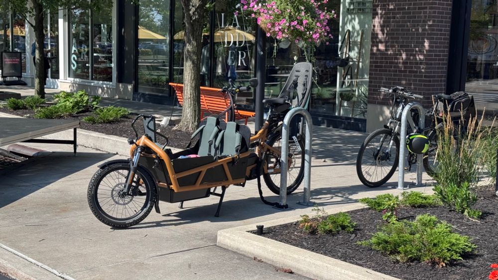 Photo of a cargo bike with two children seats in the front bucket and a child seat over the rear wheel.