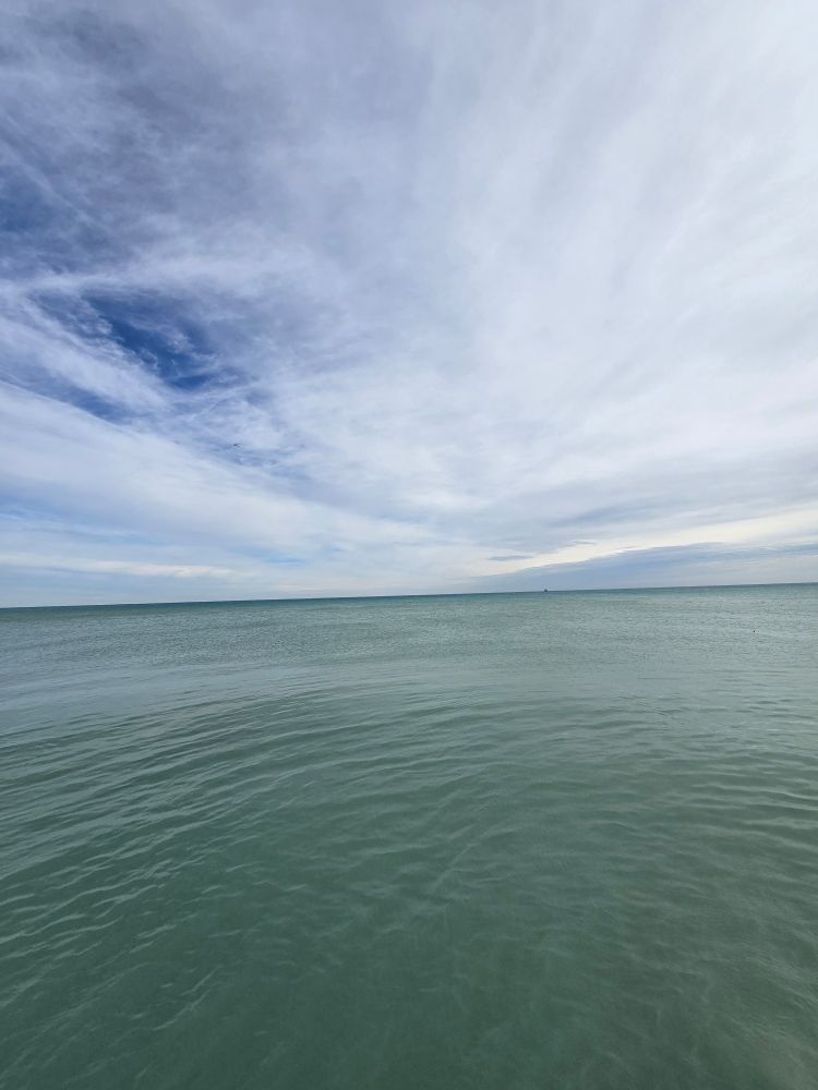 Calm, greenish-grayish Lake Michigan waters reach off into the distance and meet a partly cloudy sky at the horizon 