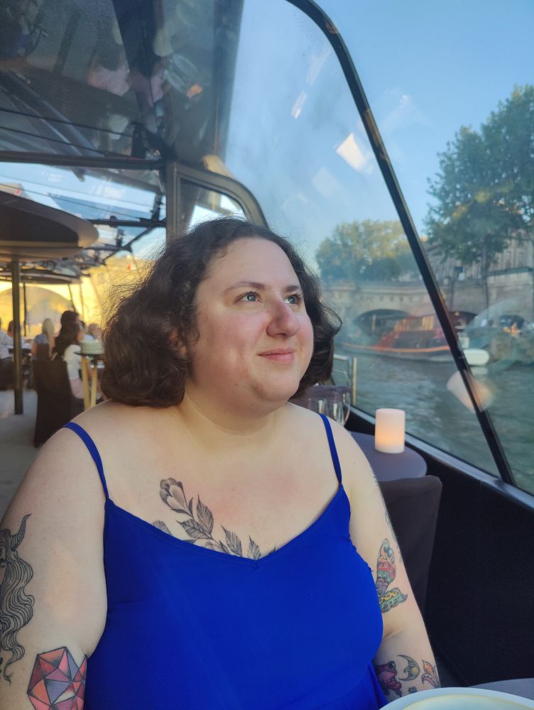 Lily looks up at the beauty of Paris from a boat on the Seine river. Her smile shows joy and wonder, and there's a glint in her eyes as though they're made of a million sparkling gems. 