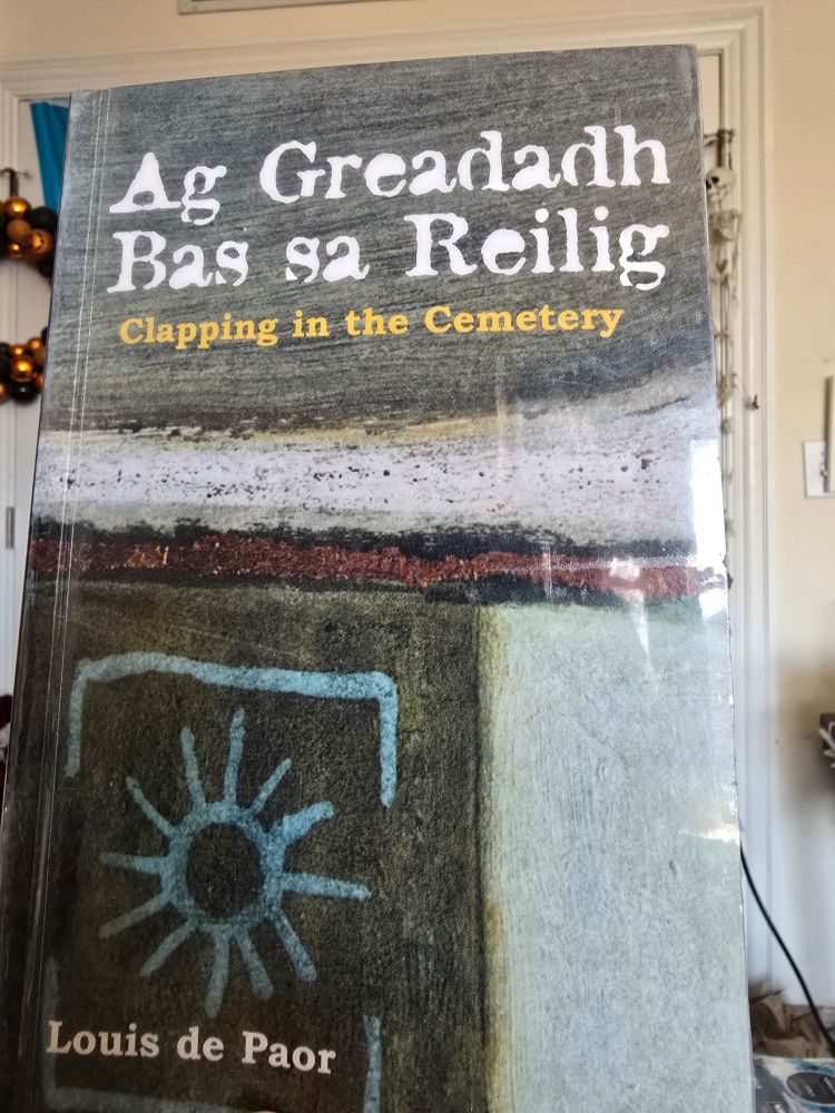 Coinním leabhar filíochta I nGaeilge. Is teideal don leabhar "Ag Greadadh Bas sa Reilig" scríofa ag Louis de Paor. 

English translation: I hold a poetry book written in Irish. The book is titled "Clapping in the Cemetery" written by Louis de Paor 