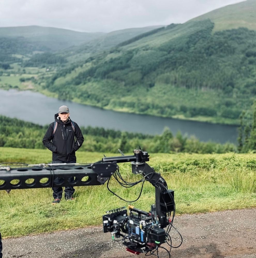 Simon Hynd and camera equipment on a hillside overlooking a reservoir. 