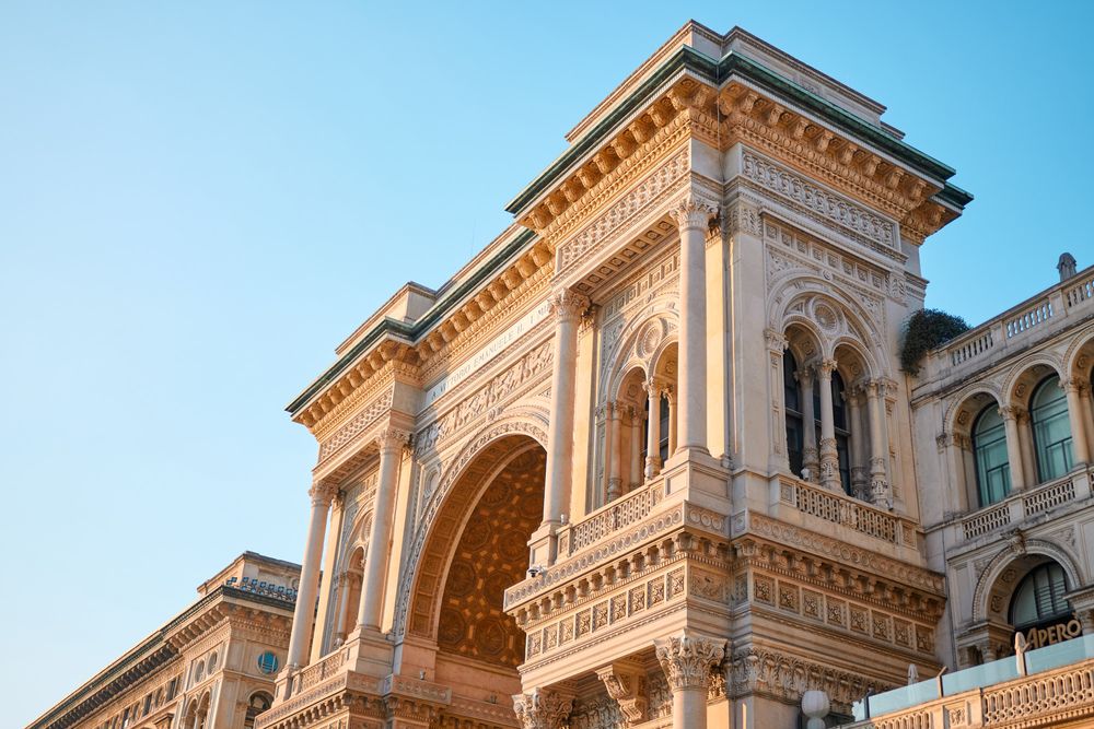 Milano - Galleria Vittorio Emanuele II. 
Ornate classical building facade with archways and decorative stonework under a blue sky.