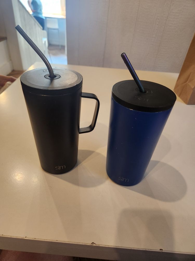 Iced lattes sitting on a table. 

Left black tumbler cup has a piña colada iced latte.

Right blue tumbler cup has a banana foster iced latte.