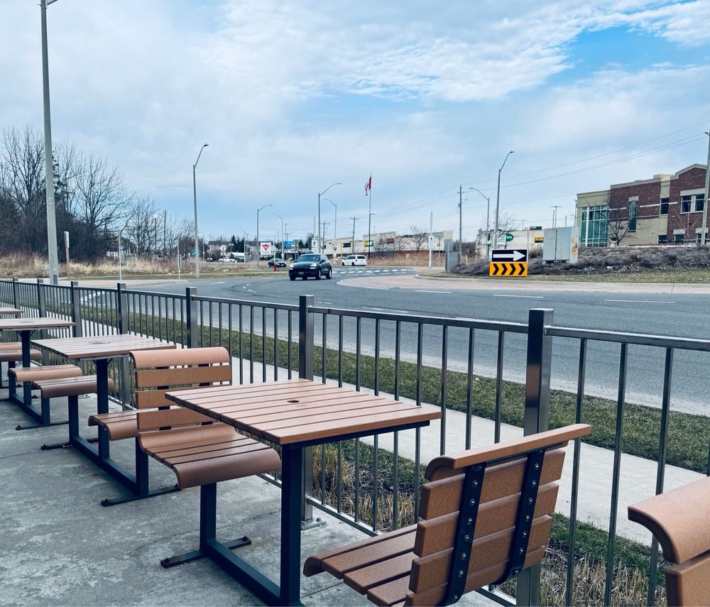 A few patio seats next tot a fence at a roundabout and a power centre in the distance 