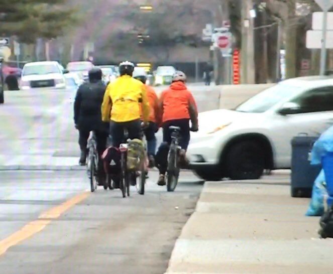 4 people on bikes riding in a contraflow lane with a driver in a white car about to cross it making a left. 