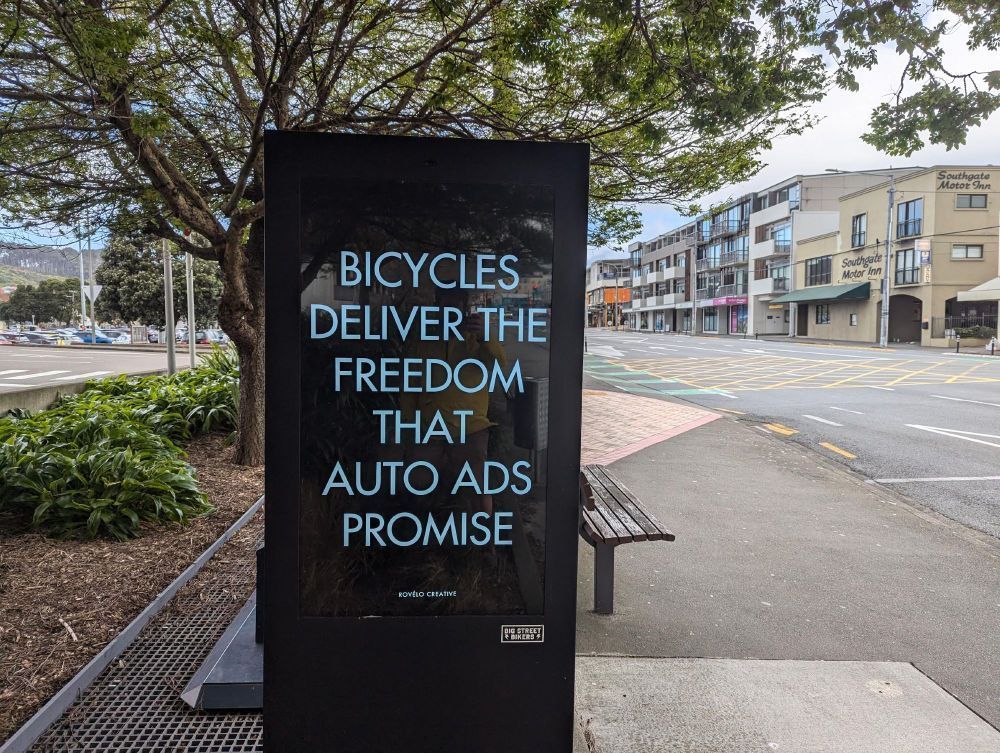 Large digital screen on a city street with Bicycles deliver the freedom that auto ads promise in white type on black