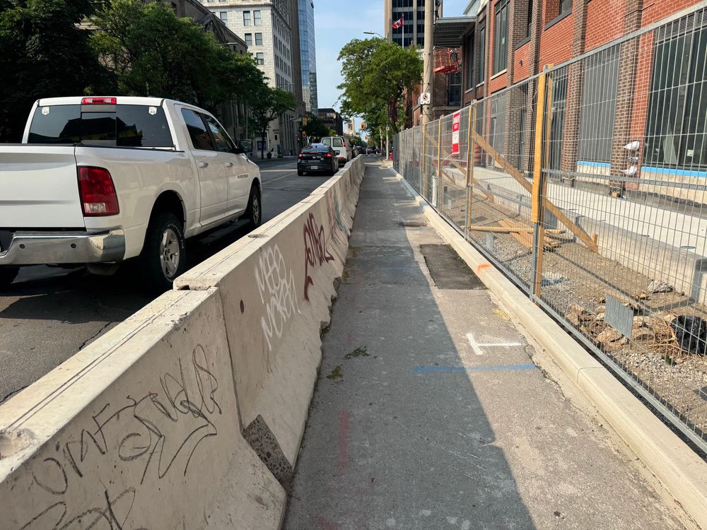 A concrete barrier on the road as construction takes over sidewalk. 