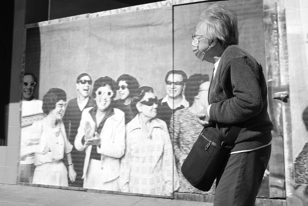 An elderly asian woman walks past Michael Jang's wheat pasted mural over the boarded up GoodWill storefront, San Francisco, CA 2021

Photo by Jessica Chen